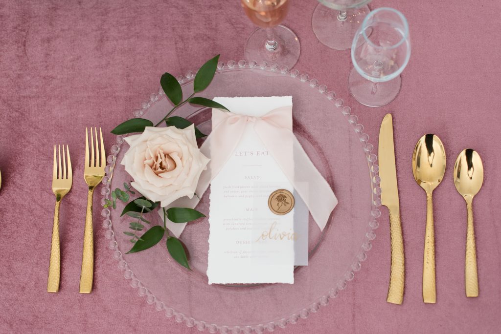 Place setting with gold flatware, a glass beaded charger plate, and hand torn menu
