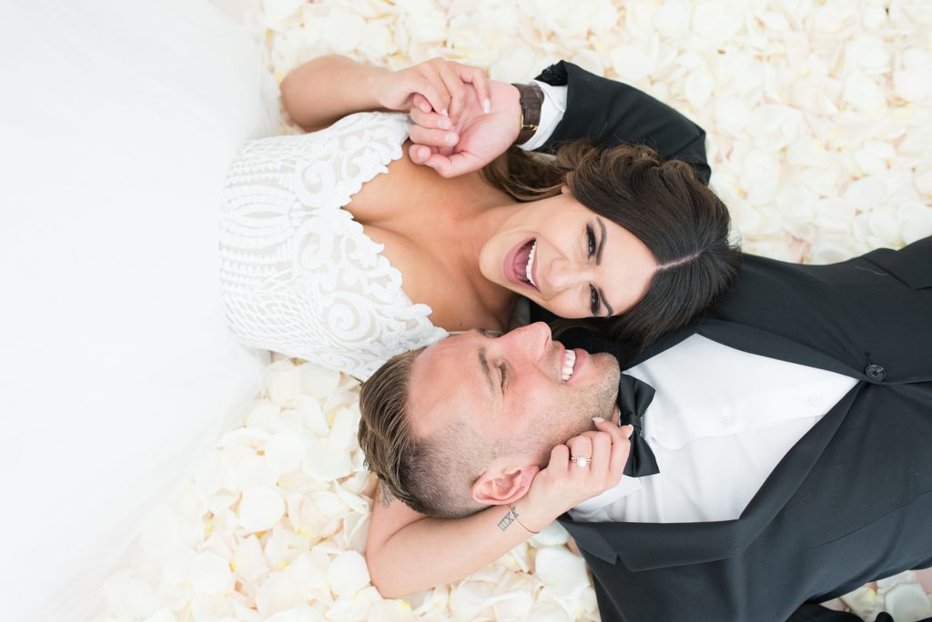 Bride and groom lay on a bed of white rose petals