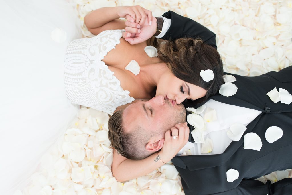 Bride and groom kissing on a bed of white rose petals