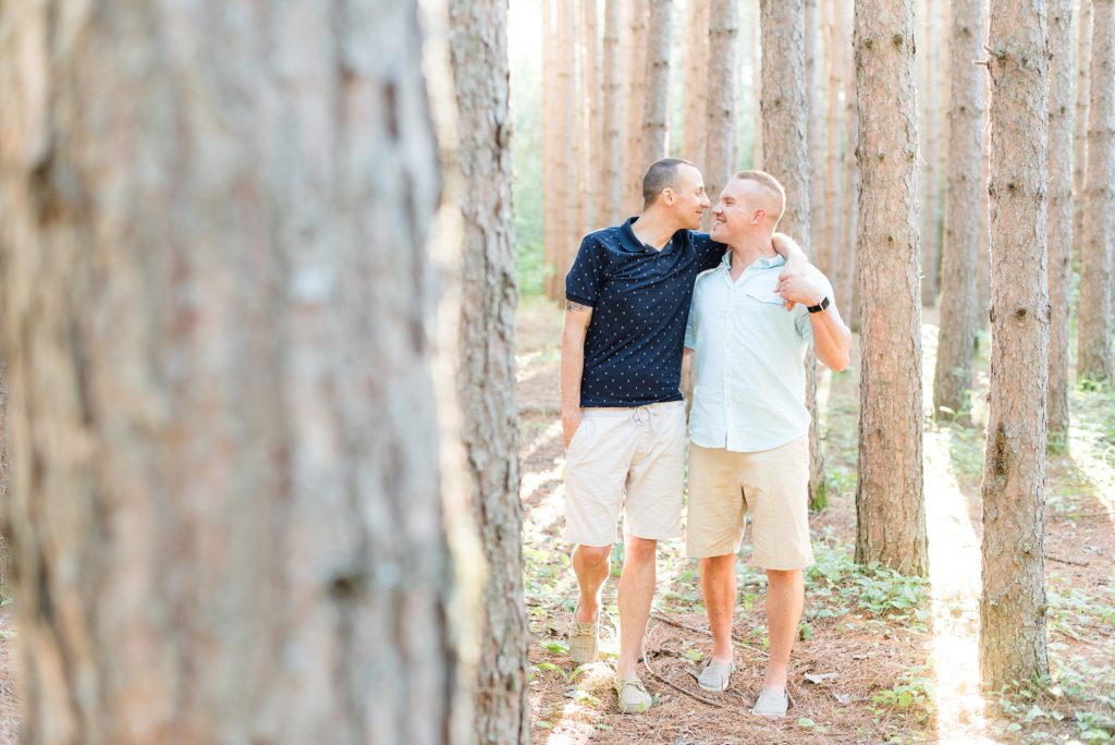 Grooms to be walk through the trees at their summer engagement session at the Thunder Bay Tree Farm
