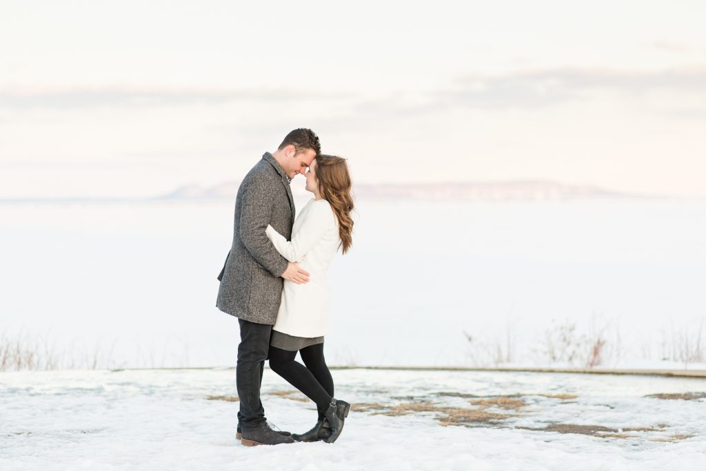 Bride and groom to be snuggle up during their winter engagement session as they pose in front of the sleeping giant as seen from Marina Park in Thunder Bay