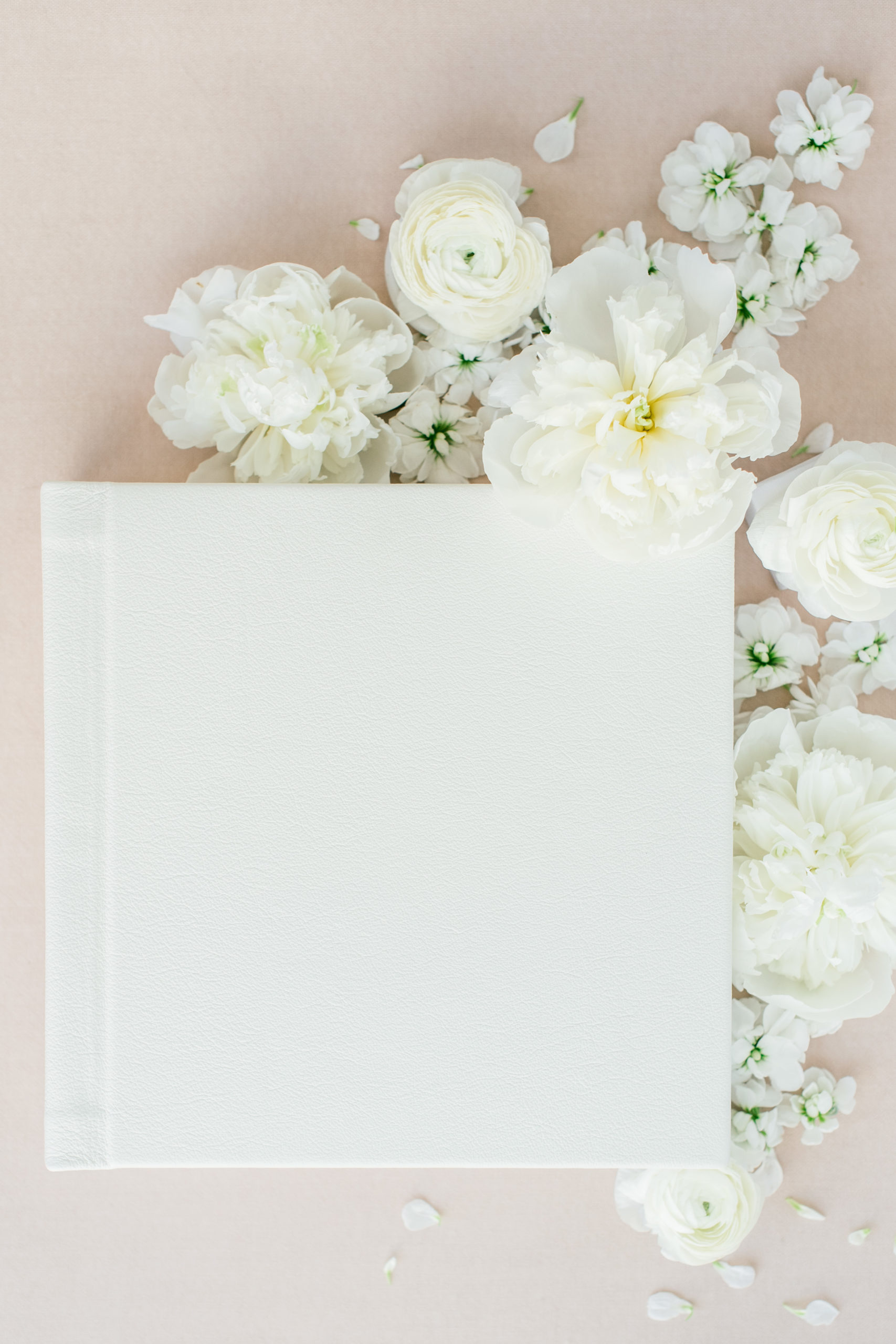 A white leather wedding album surrounded by flowers