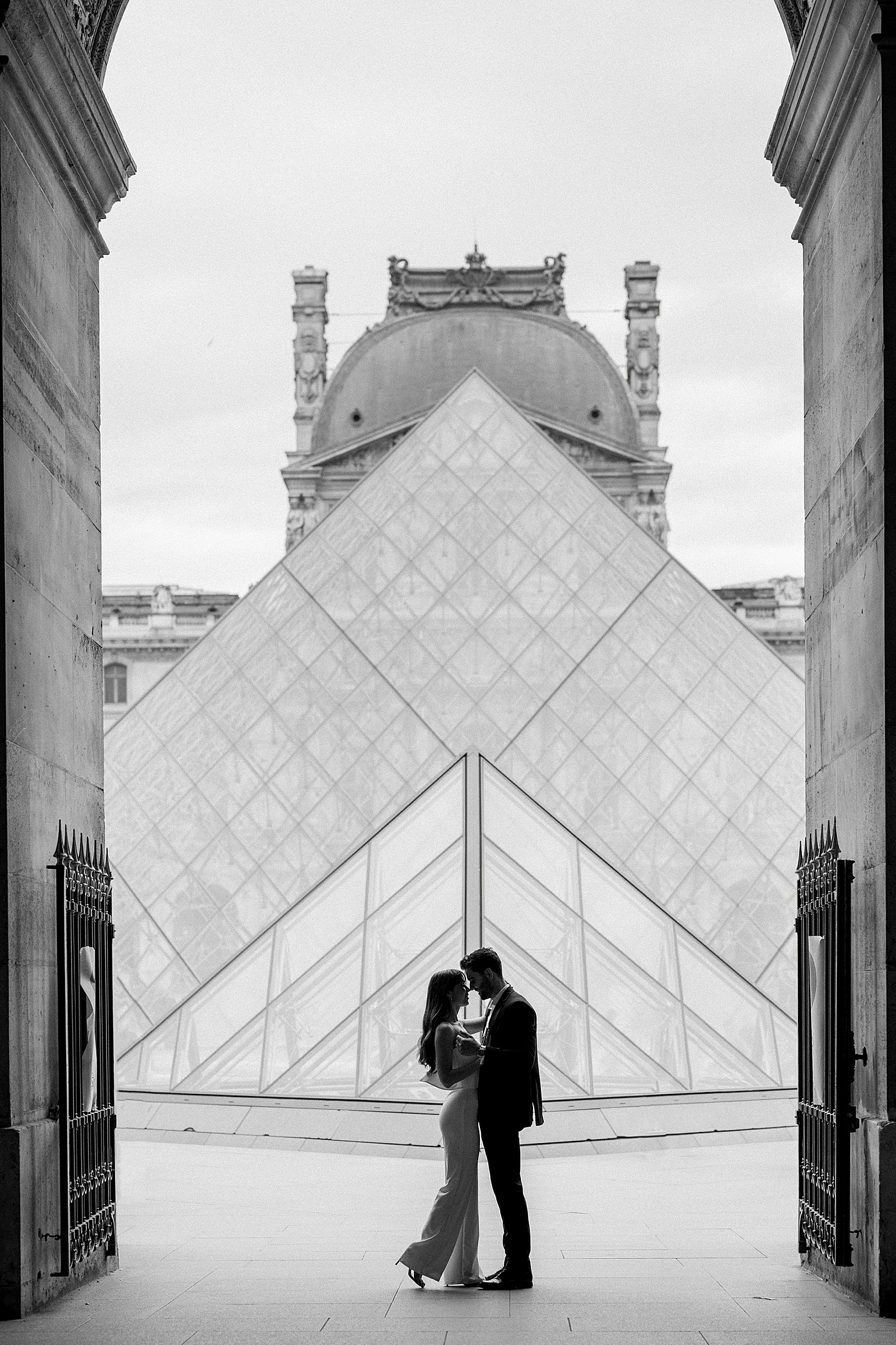 A couple is silhouetted against the glass triangle dome of the Louvre