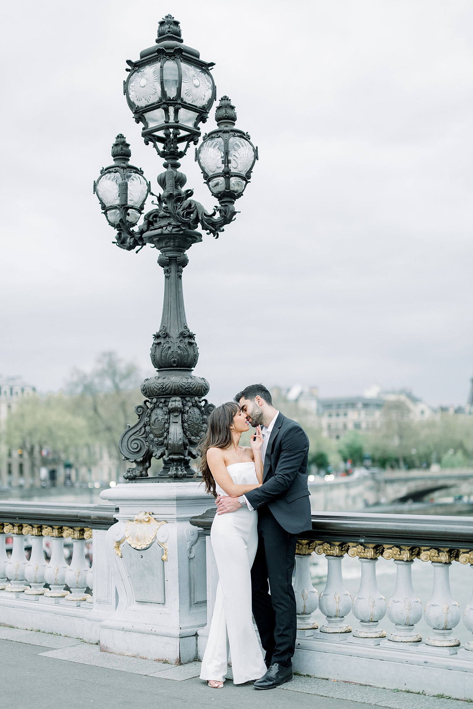 A couple snuggles up by one of the lamp posts on the Pont Alexandre III