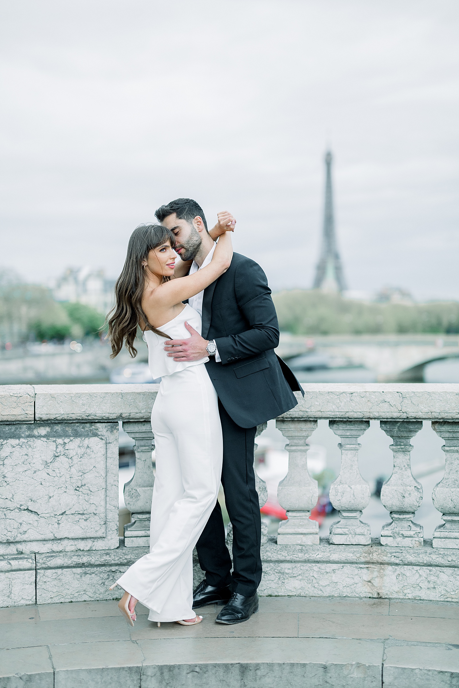 A couple cuddles up on the pont alexandre iii with the eiffle tower in the distance