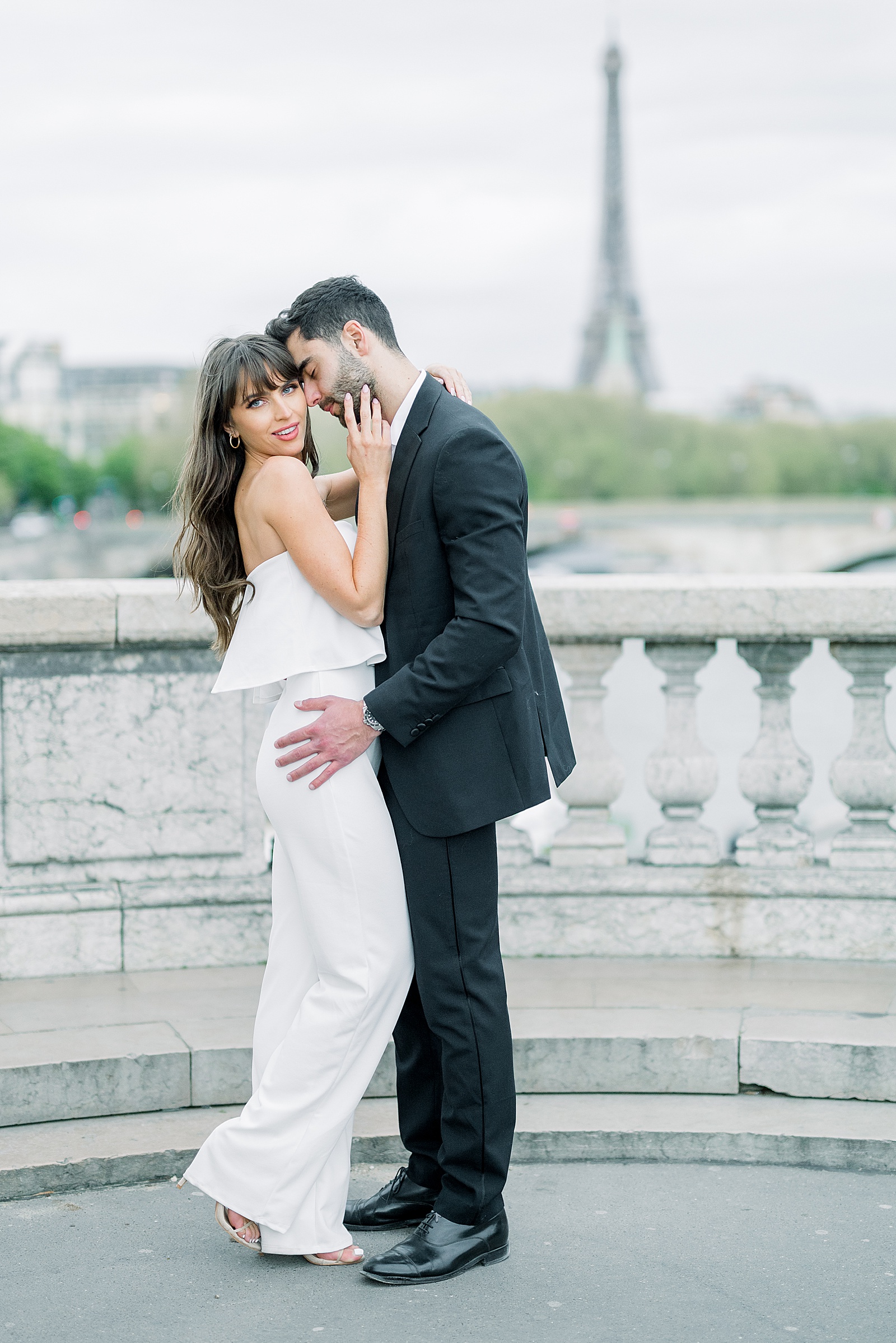 A couple stands on the pont alexandre iii with the Eiffel tower in the distance