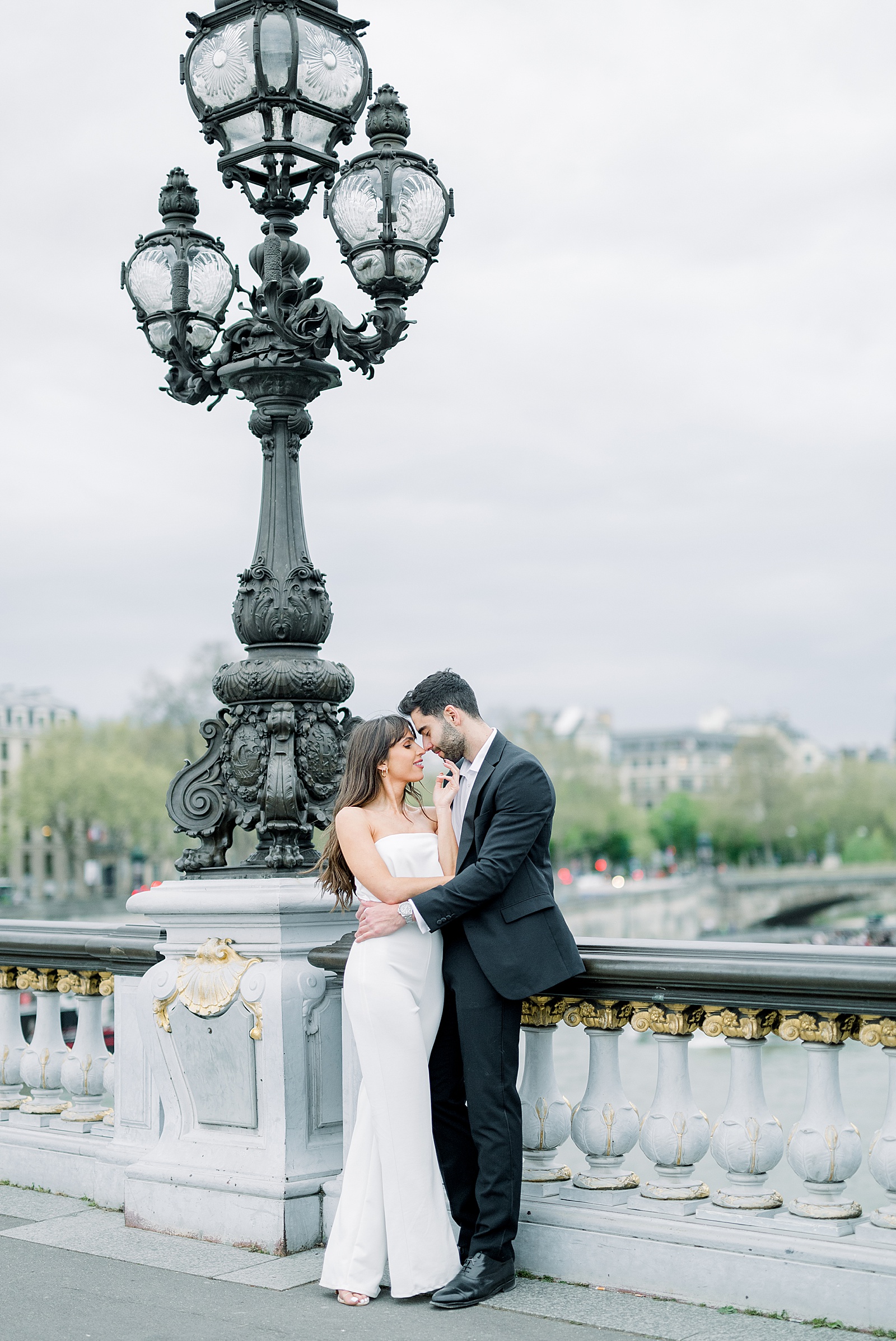 A couple stands by one of the lamp posts on the pont alexandre iii