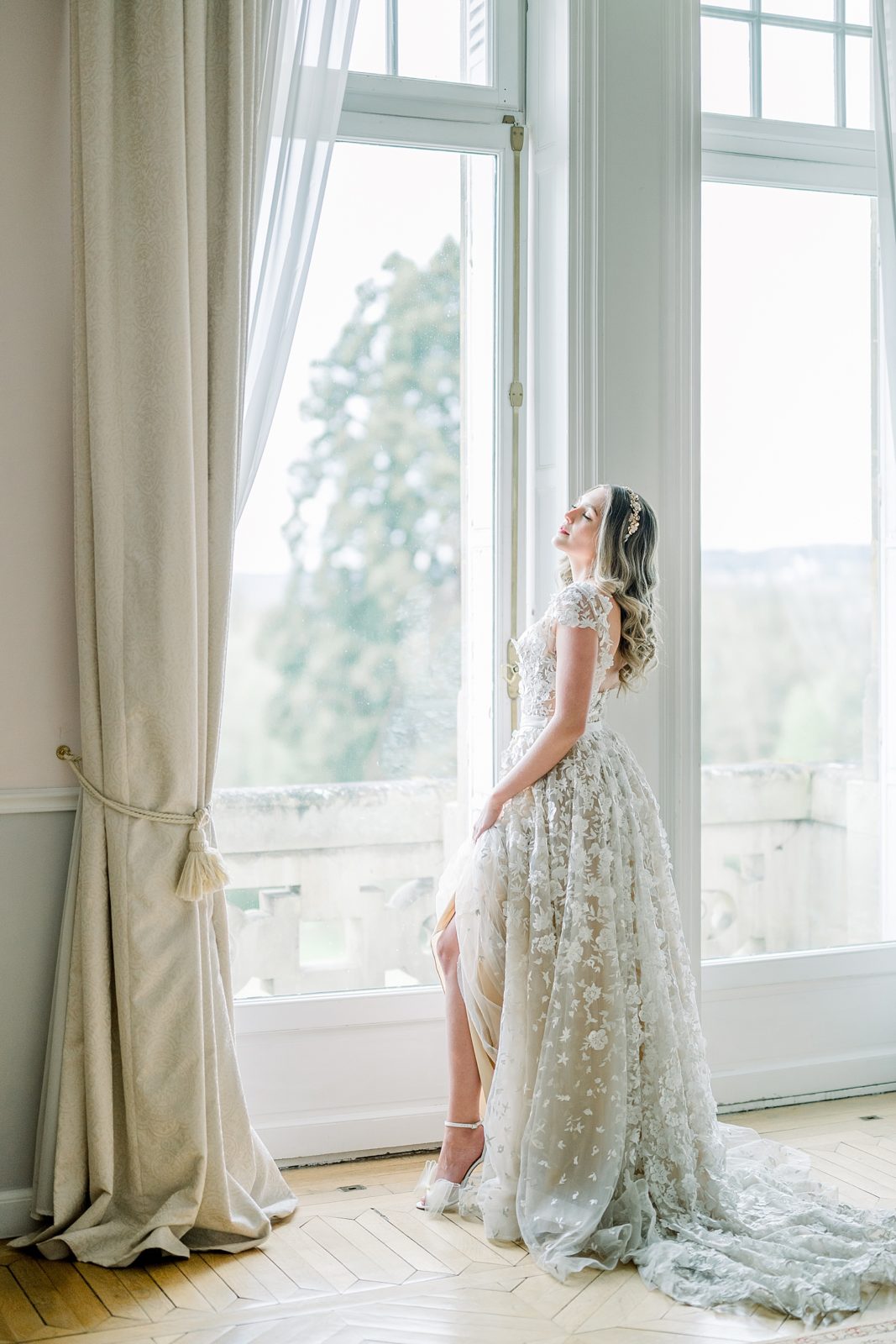 Bride standing by a window inside Chateau Bouffemont showing off her Jimmy Choo wedding shoes