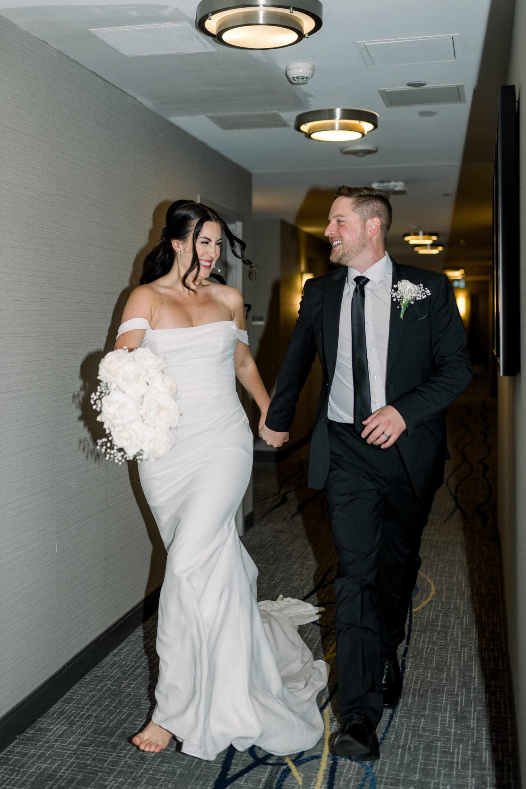 Bride and groom holding hands running down the hallway of the Delta Hotel in Thunder Bay