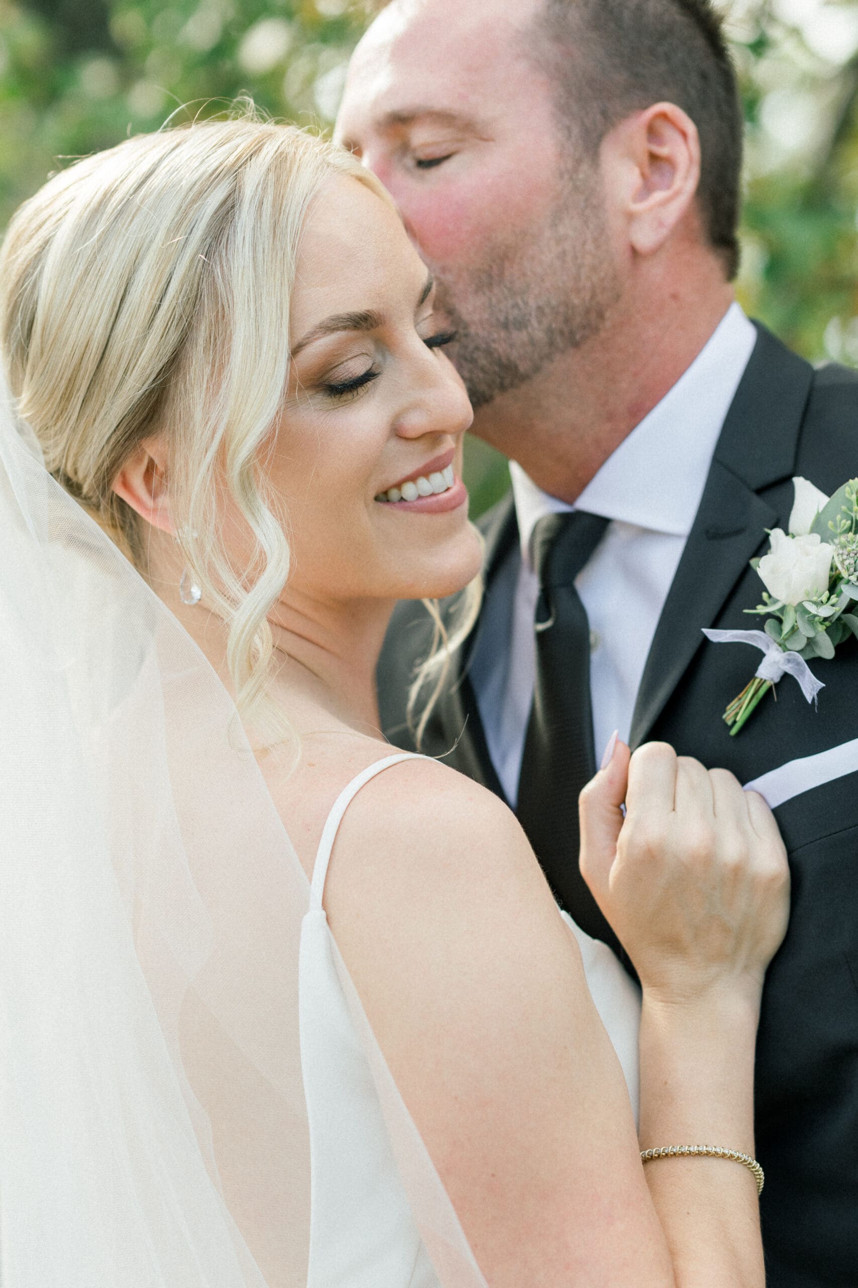 Groom kissing bride on the temple while she holds on to his lapels